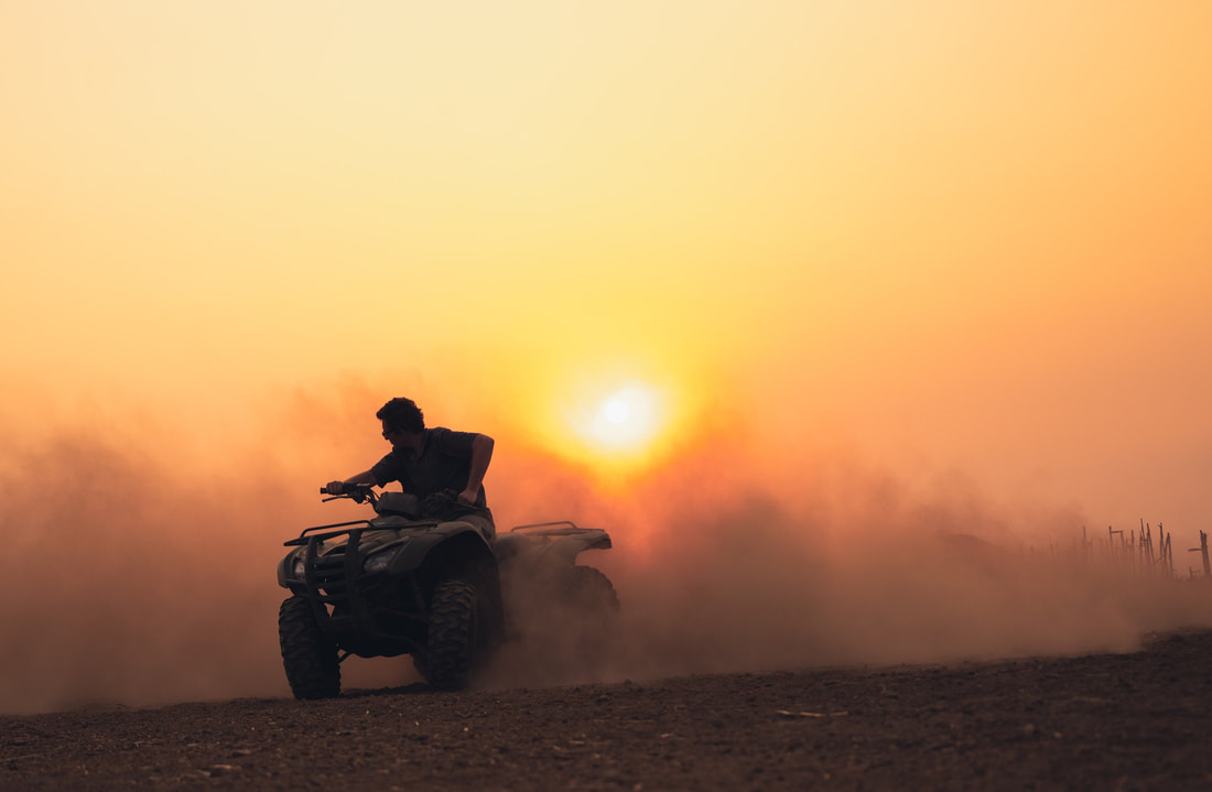 Man cruising on an ATV in a dirt lot on a farm in Utah during sunset.